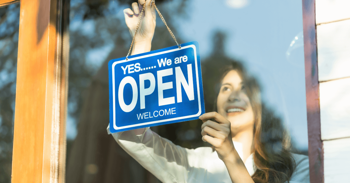 A woman hanging an open sign on a business door.