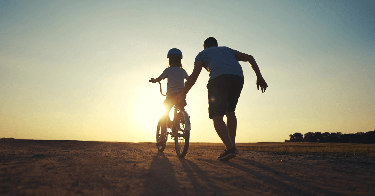 A man helping a child ride a bike.