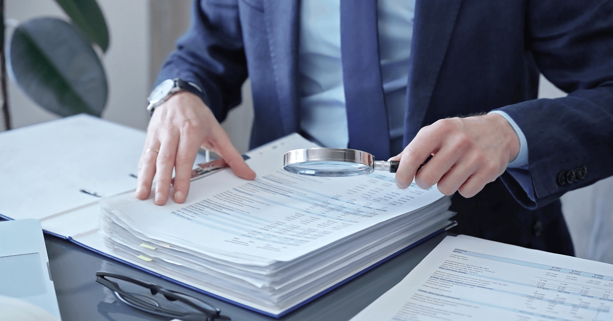 A man examining reports with a magnifying glass.