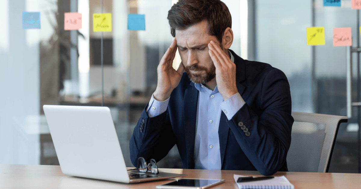 A man on a laptop holding his head in pain.